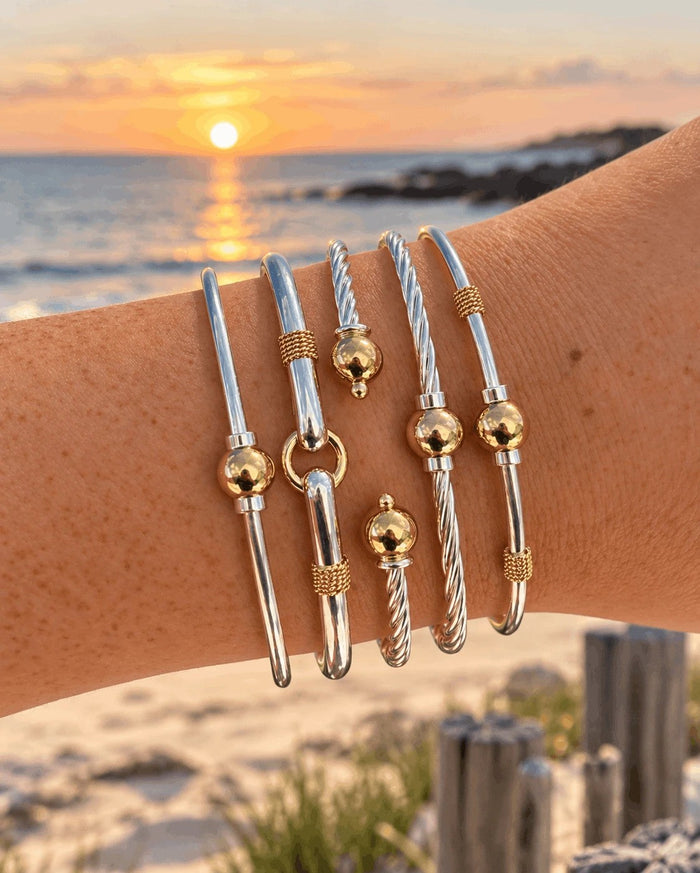 A stack of sterling silver and 14k gold filled Coastal ball bracelets at sunset on the beach